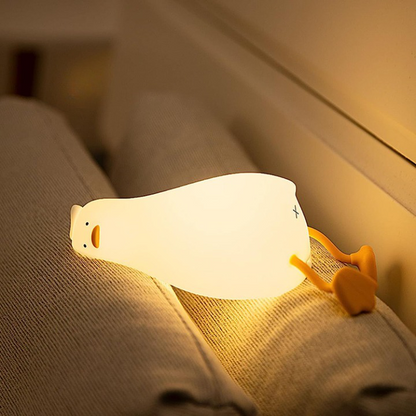 La veilleuse canard Ducky illuminée sur deux coussins dans une chambre d'enfant.